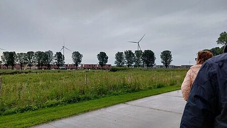 Foto van een landschap met windmolens in de verte en personen op de voorgrond, op de rug gezien